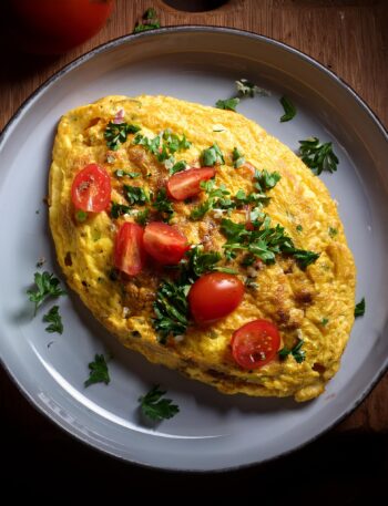 Fluffy omelette filled with cheese, mushrooms, and fresh herbs served on a plate