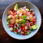 Fresh ceviche with diced fish, colorful vegetables, and a garnish of cilantro and lime wedges.