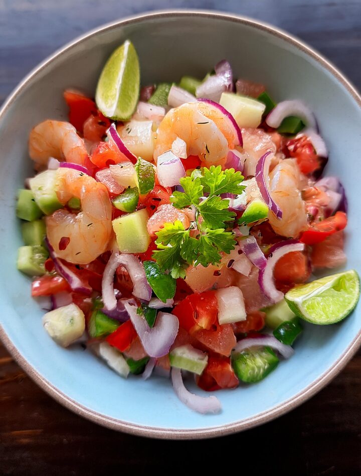 Fresh ceviche with diced fish, colorful vegetables, and a garnish of cilantro and lime wedges.