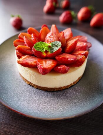 A layered strawberry cheesecake cake with fresh strawberries and creamy frosting